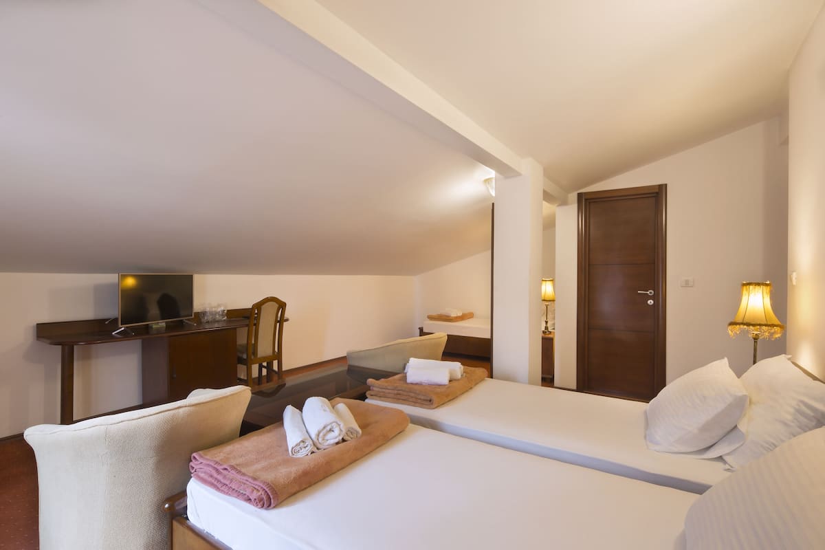 A hotel room with two beds, a desk, a chair, and a television.