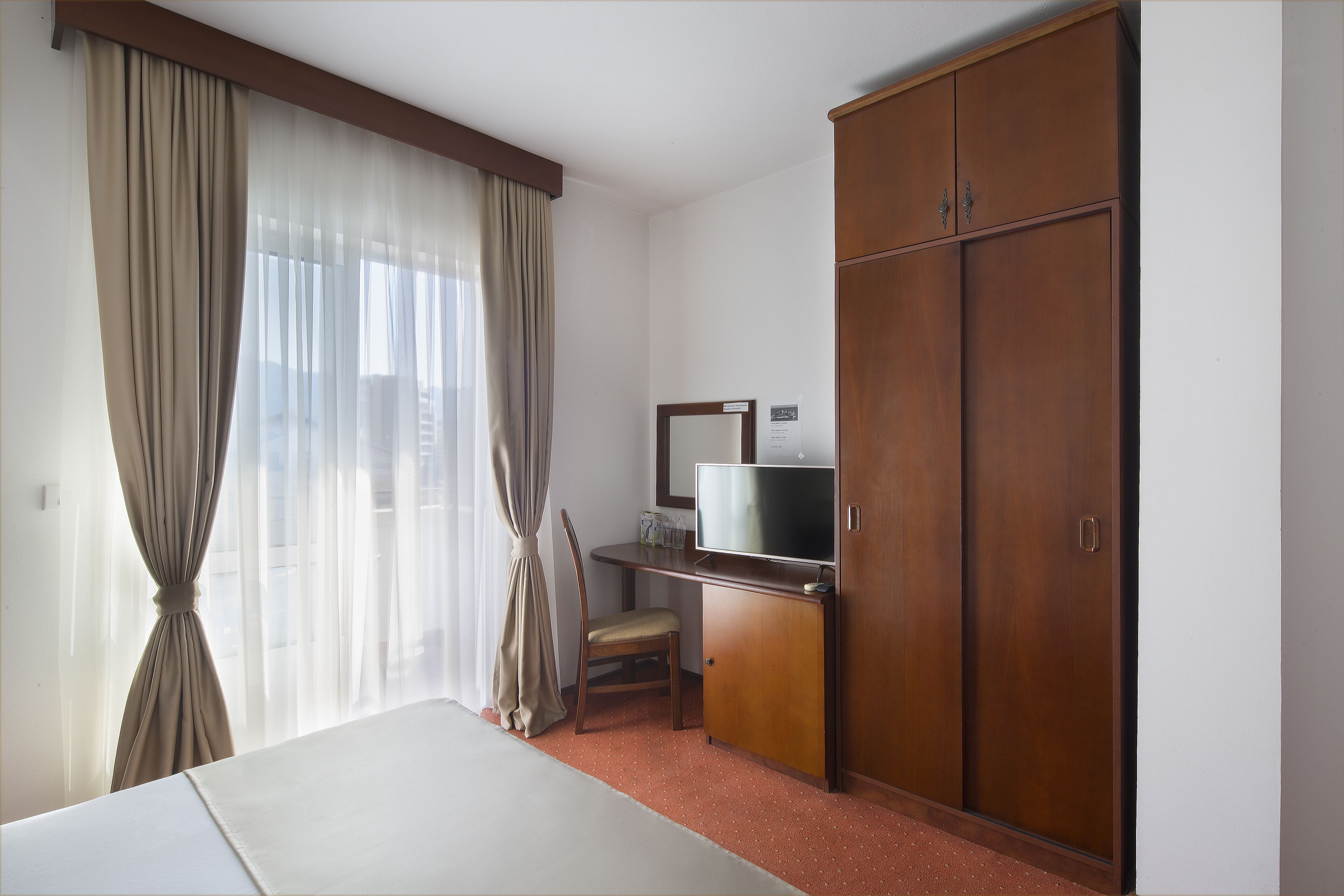 Una habitación de hotel con cama, escritorio con televisor, armario y una silla.