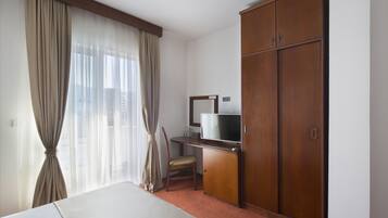 Una habitación de hotel con cama, escritorio con televisor, armario y una silla.