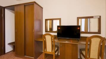 A room with a wooden desk, a television, two chairs, and a wardrobe.