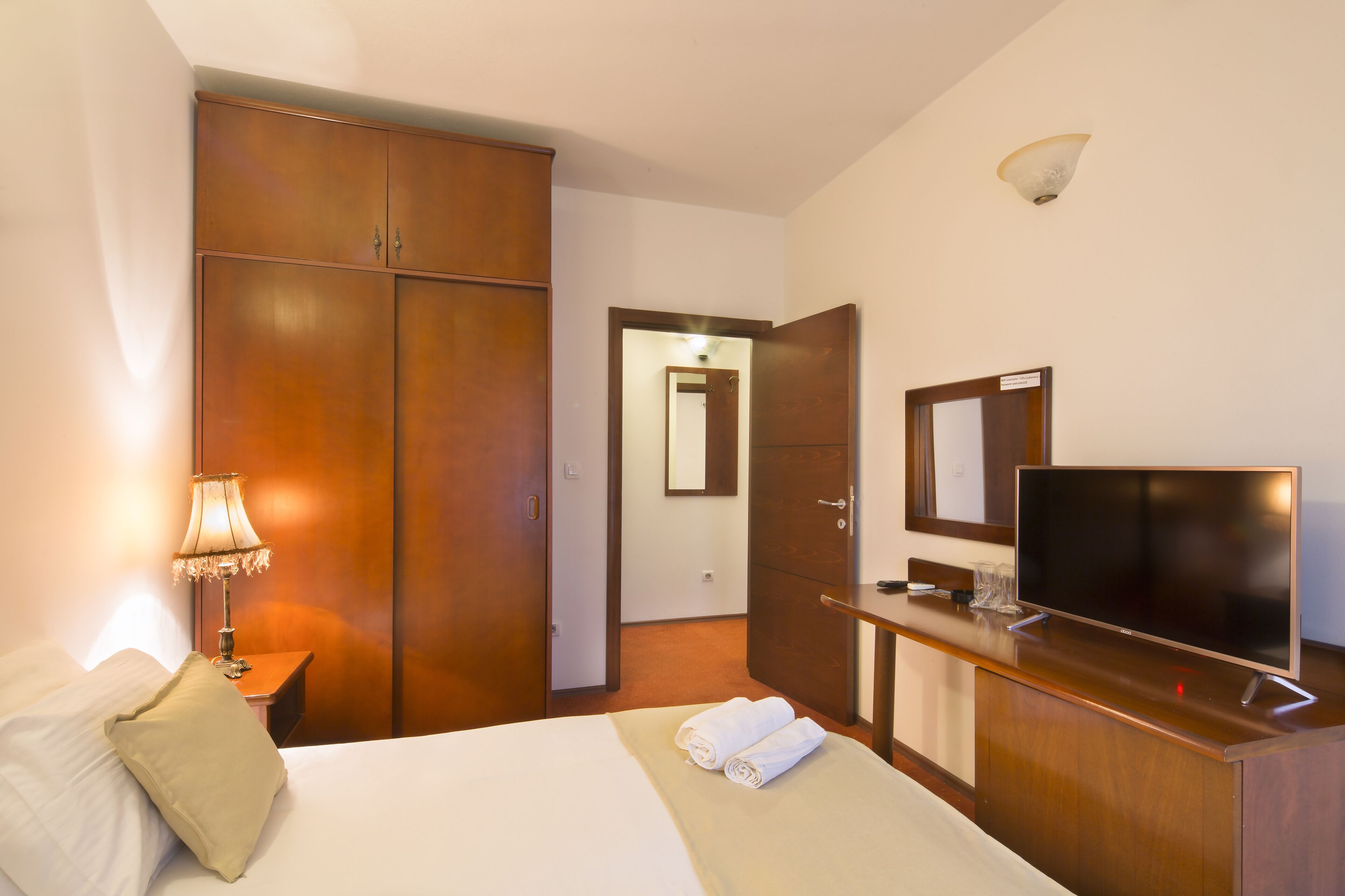 Una habitación de hotel con cama, televisión, armario y escritorio con lámpara.