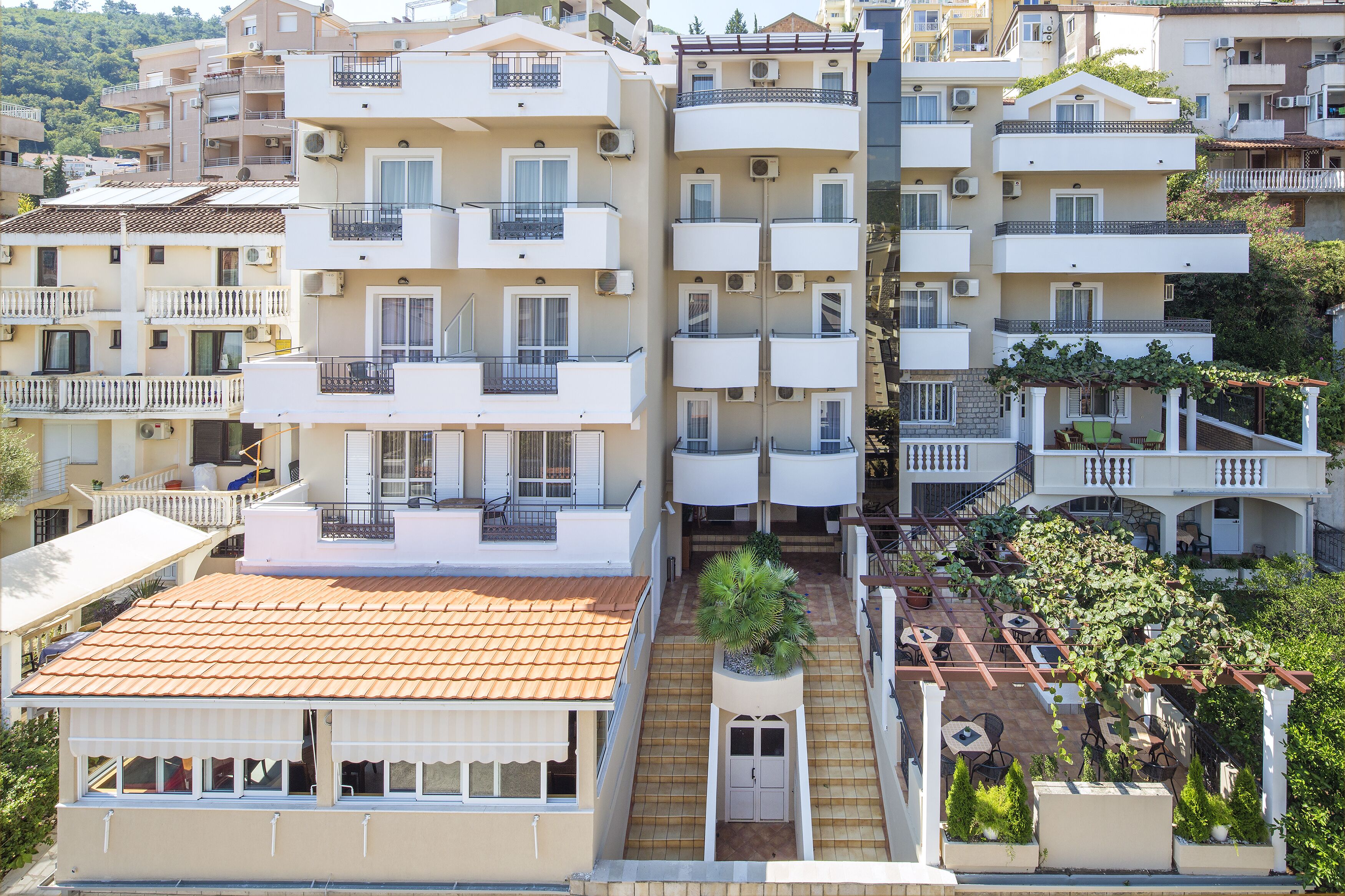 A multi-story residential building with balconies, a rooftop terrace, and a small garden area.