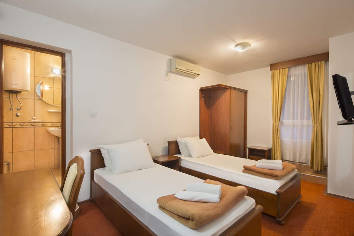 A hotel room with two single beds, a wooden wardrobe, a desk, and a television.