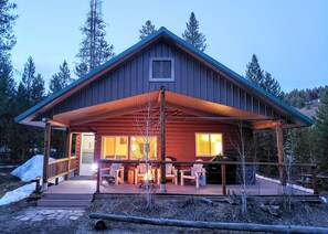A wooden cabin with a covered porch, a fireplace, and a view of the surrounding forest. - Stanley Stays - The Valley Creek Cabin (Stanley)