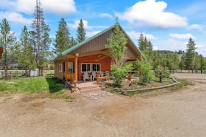 A log cabin with a porch, outdoor seating, and a view of a forested area. - Stanley Stays - The Valley Creek Cabin (Stanley)