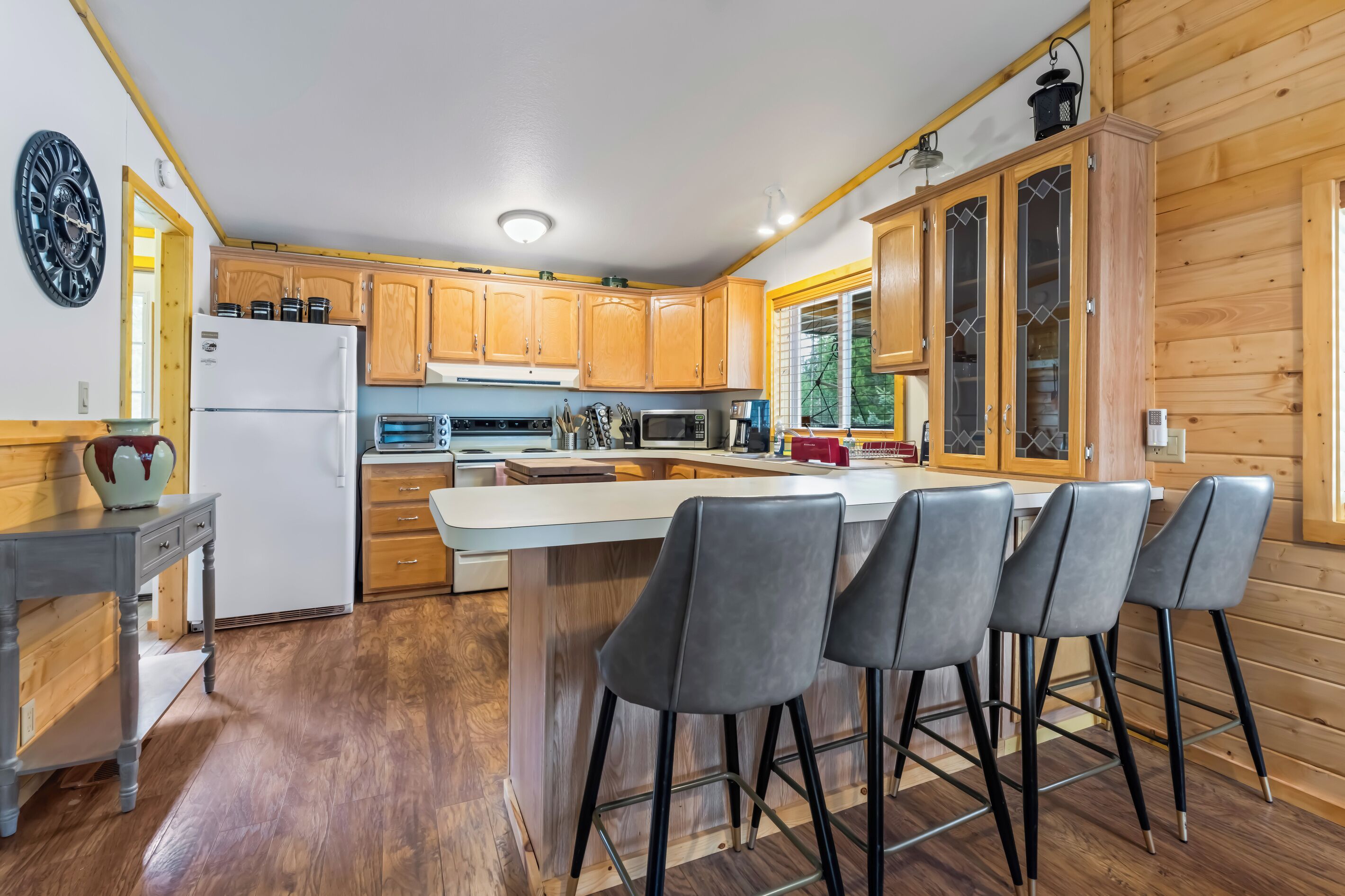 A modern kitchen with wooden cabinets, a central island with bar stools, a refrigerator, and a microwave.