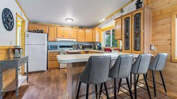 A modern kitchen with wooden cabinets, a central island with bar stools, a refrigerator, and a microwave.