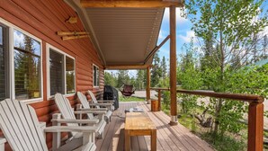 Una terraza de madera con sillas Adirondack y una mesa, con vistas a una zona boscosa.