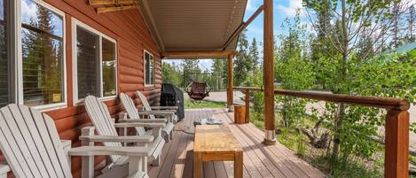 A wooden deck with Adirondack chairs and a table, overlooking a forested area.