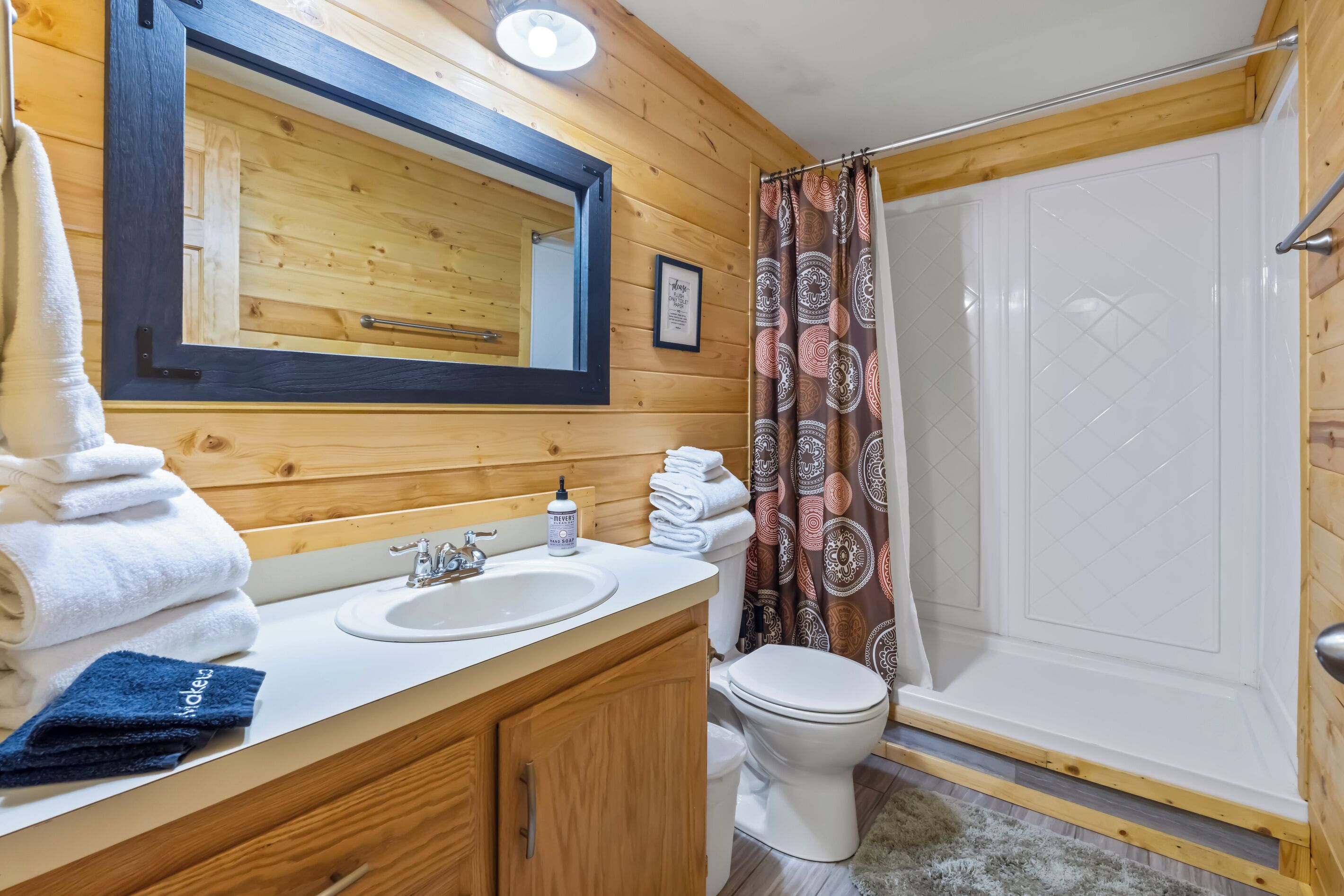 A wooden cabin bathroom with a sink, mirror, toilet, and shower.