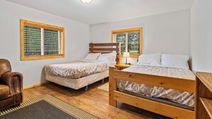 Un dormitorio con dos camas de madera, un sillón de cuero marrón y una ventana con persianas.