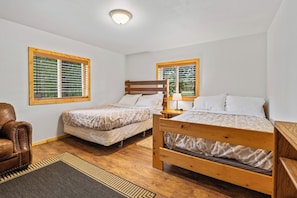 A bedroom with two wooden beds, a brown leather chair, and a window with blinds. - Stanley Stays - The Valley Creek Cabin (Stanley)