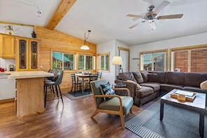 A spacious living area with a wooden floor, a dining table with chairs, a sofa, and a ceiling fan. - Stanley Stays - The Valley Creek Cabin (Stanley)