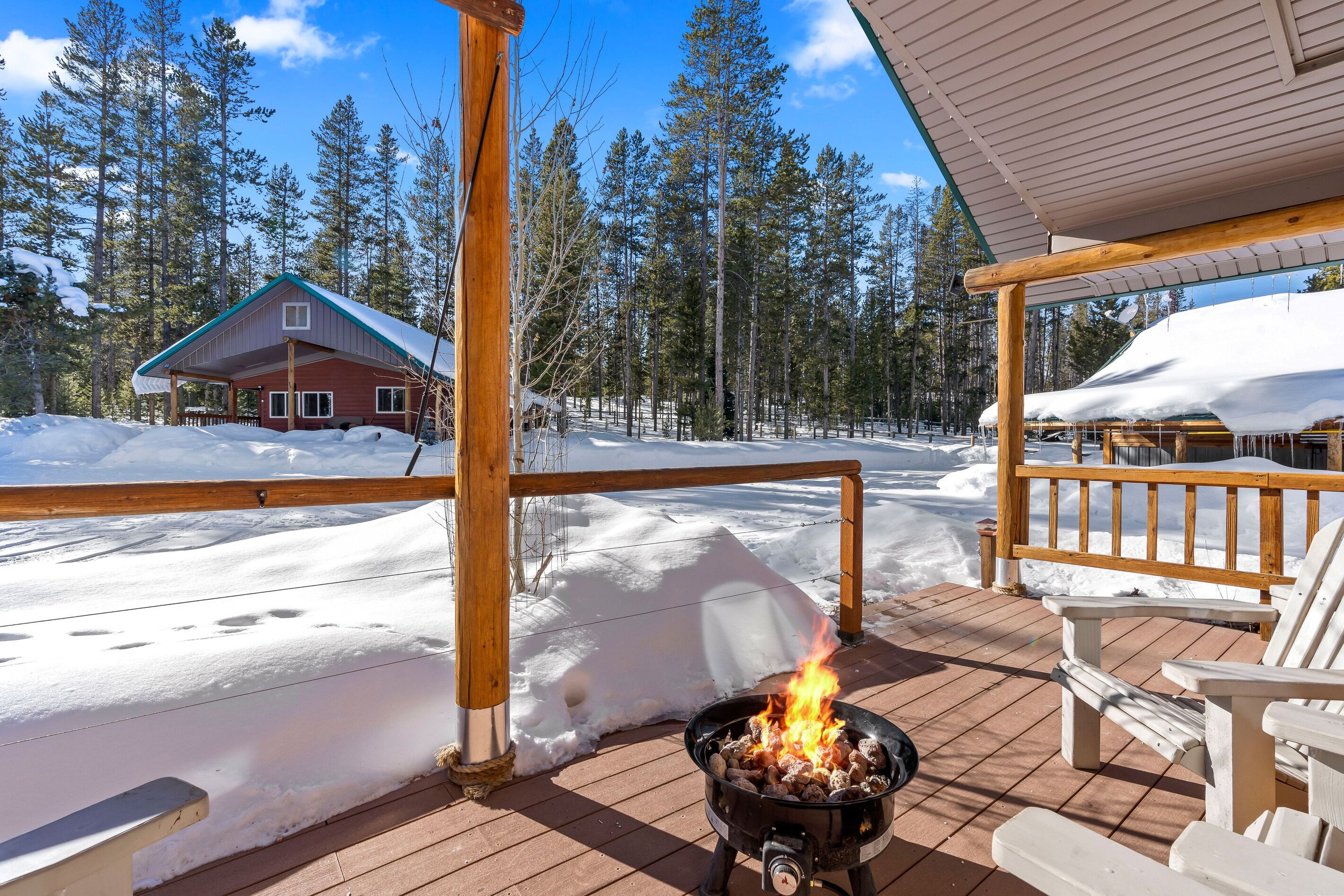 A wooden deck with a fire pit, snow-covered ground, and a cabin in the background.