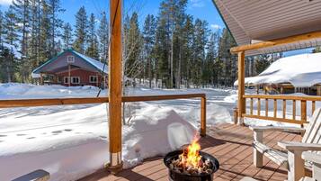 A wooden deck with a fire pit, snow-covered ground, and a cabin in the background.