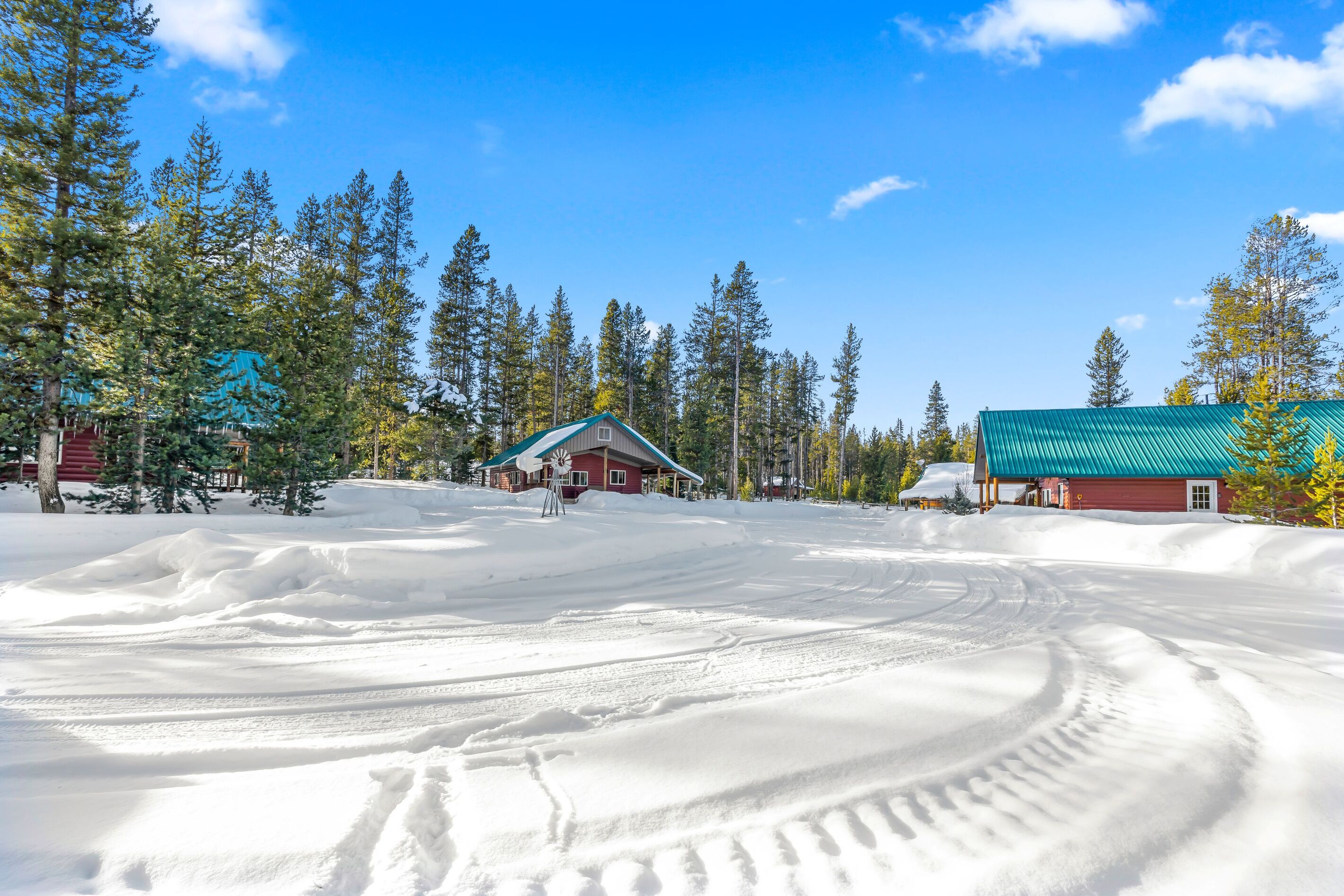 A snow-covered landscape with a red building and a windmill, surrounded by trees.