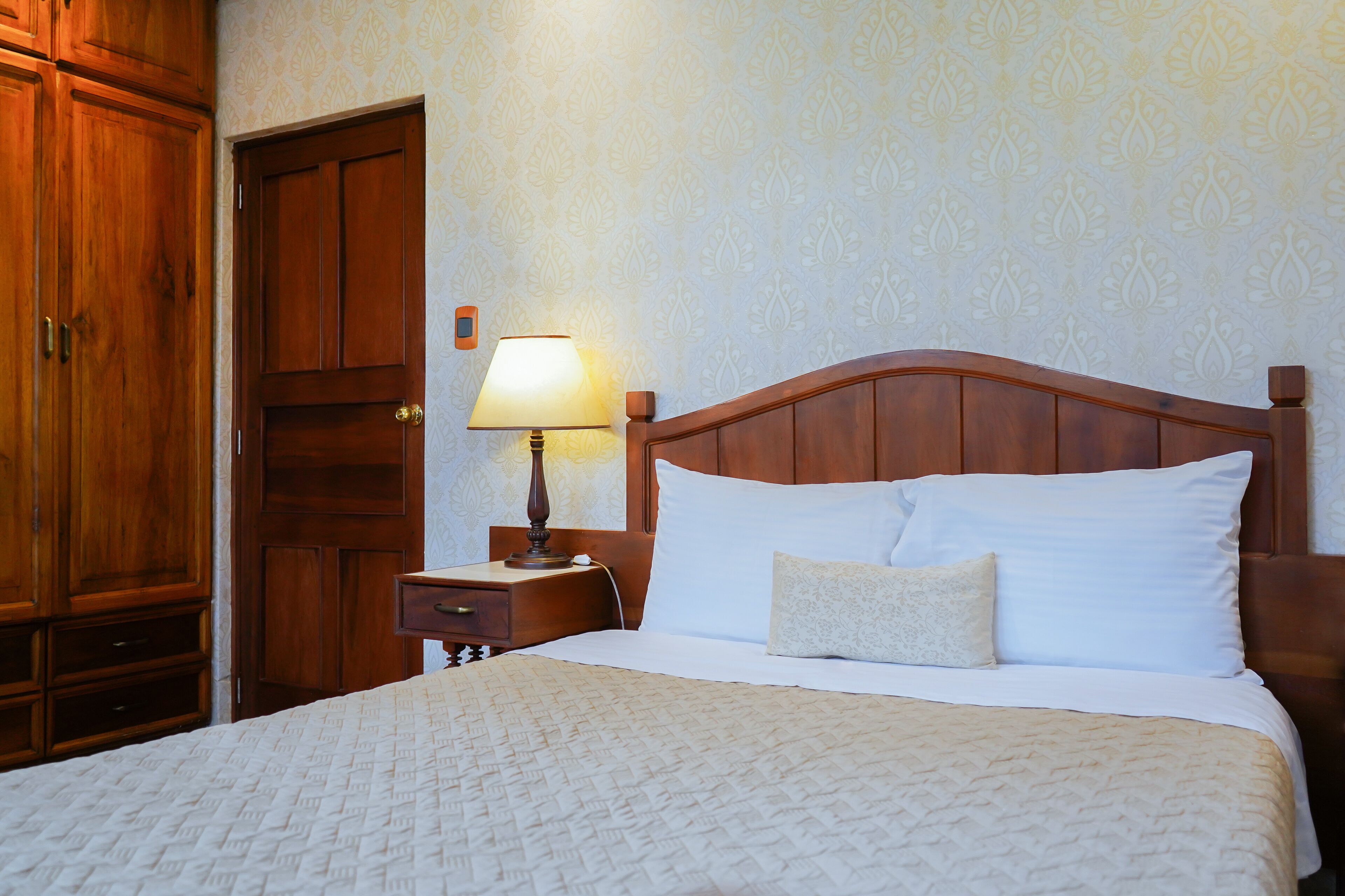 A neatly made bed with a wooden headboard, a bedside table with a lamp, and a wardrobe.