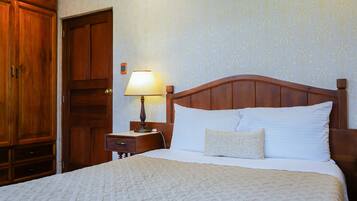 A neatly made bed with a wooden headboard, a bedside table with a lamp, and a wardrobe.