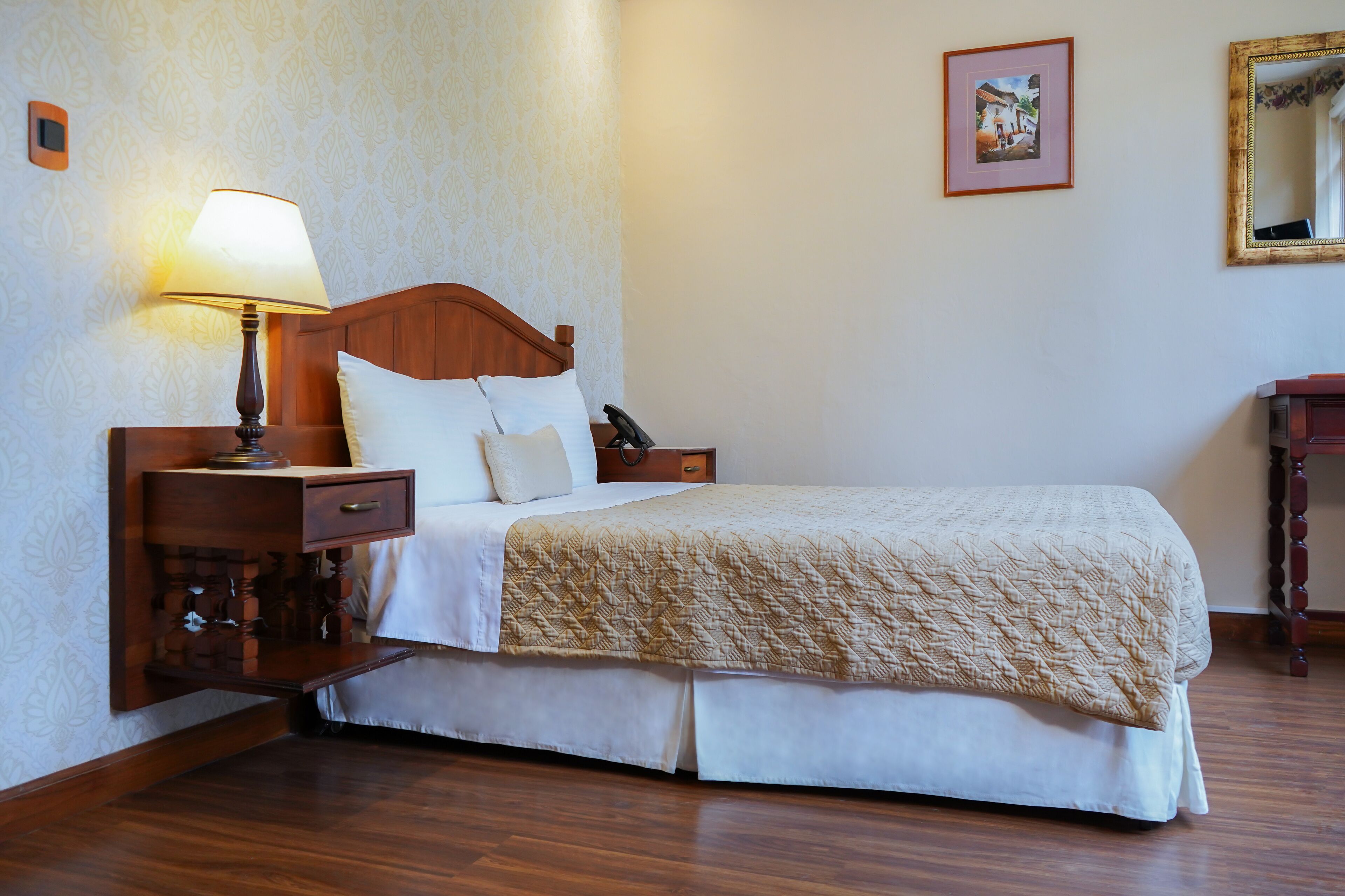 Una cama bien hecha con cabecera de madera, una lámpara de noche y una mesita de noche con un cajón.