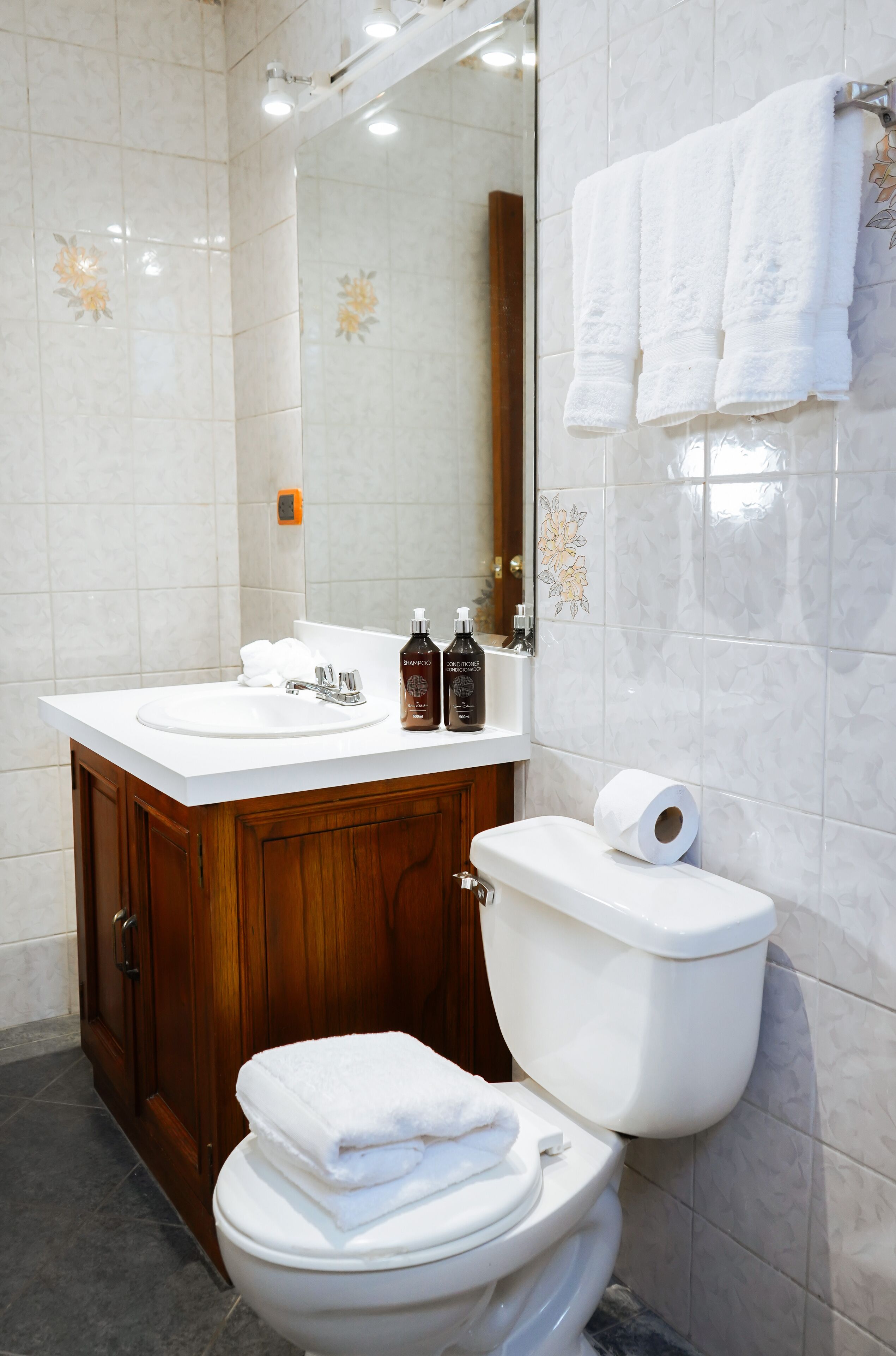 Ein Badezimmer mit einem weißen Waschbecken, einem Holzkonsolenunterschrank und einer Toilette.