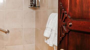 A bathroom with a wooden door, a towel rack, a glass shelf with toiletries, and a shower area.
