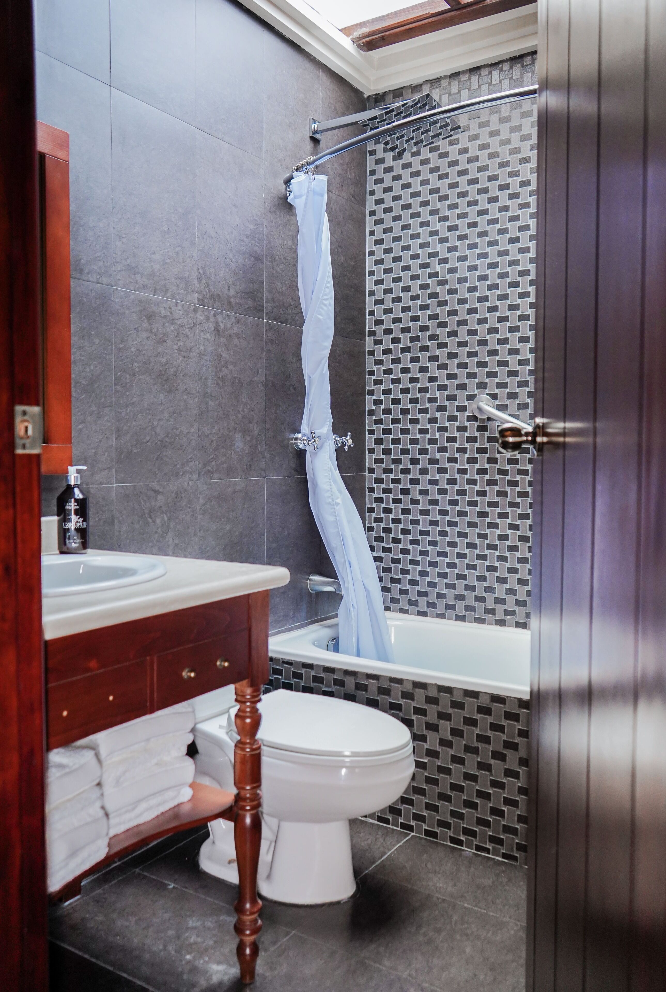 A bathroom with a white toilet, a wooden vanity with a mirror, a sink, and a shower area with a tiled wall.