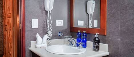 Un baño con un lavamanos blanco, un secador de pelo y artículos de aseo en la encimera.