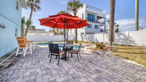 A patio with a pool table, chairs, and a red umbrella. - Upper-Level 2BR | Pool, Private Deck & 2-Min Walk to Beach and Flagler Avenue (New Smyrna Beach)