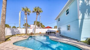 A swimming pool with a curved edge, surrounded by a brick patio and palm trees. - Upper-Level 2BR | Pool, Private Deck & 2-Min Walk to Beach and Flagler Avenue (New Smyrna Beach)