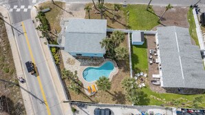 An aerial view of a property with a swimming pool, a guesthouse, and a large building with a grey roof. - Upper-Level 2BR | Pool, Private Deck & 2-Min Walk to Beach and Flagler Avenue (New Smyrna Beach)