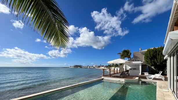 Una piscina trasparente con vista sul mare, un'area relax con ombrelloni e un edificio con la scritta 'ZONIN'.