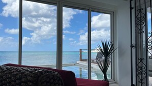 Una stanza con un'ampia porta scorrevole in vetro che dà su un balcone con vista sull'oceano e su una piscina.