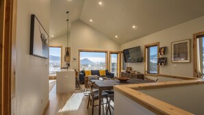 A modern kitchen with wooden countertops, a dining area with a table and chairs, and large windows offering a view of mountains.