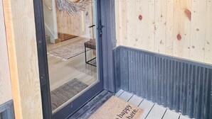 A wooden exterior with a black-framed door, a doormat with text, and a light fixture on the wall.
