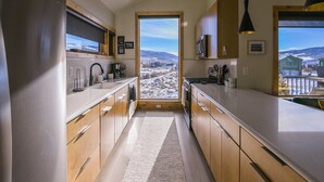 A modern kitchen with wooden cabinets, stainless steel appliances, and a view of a snowy landscape through a doorway.