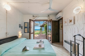 A bedroom with a bed, a ceiling fan, a view through an open door, and wall-mounted lights.