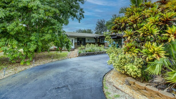 Une allée sinueuse mène à une maison entourée d’une végétation luxuriante et de plantes tropicales.