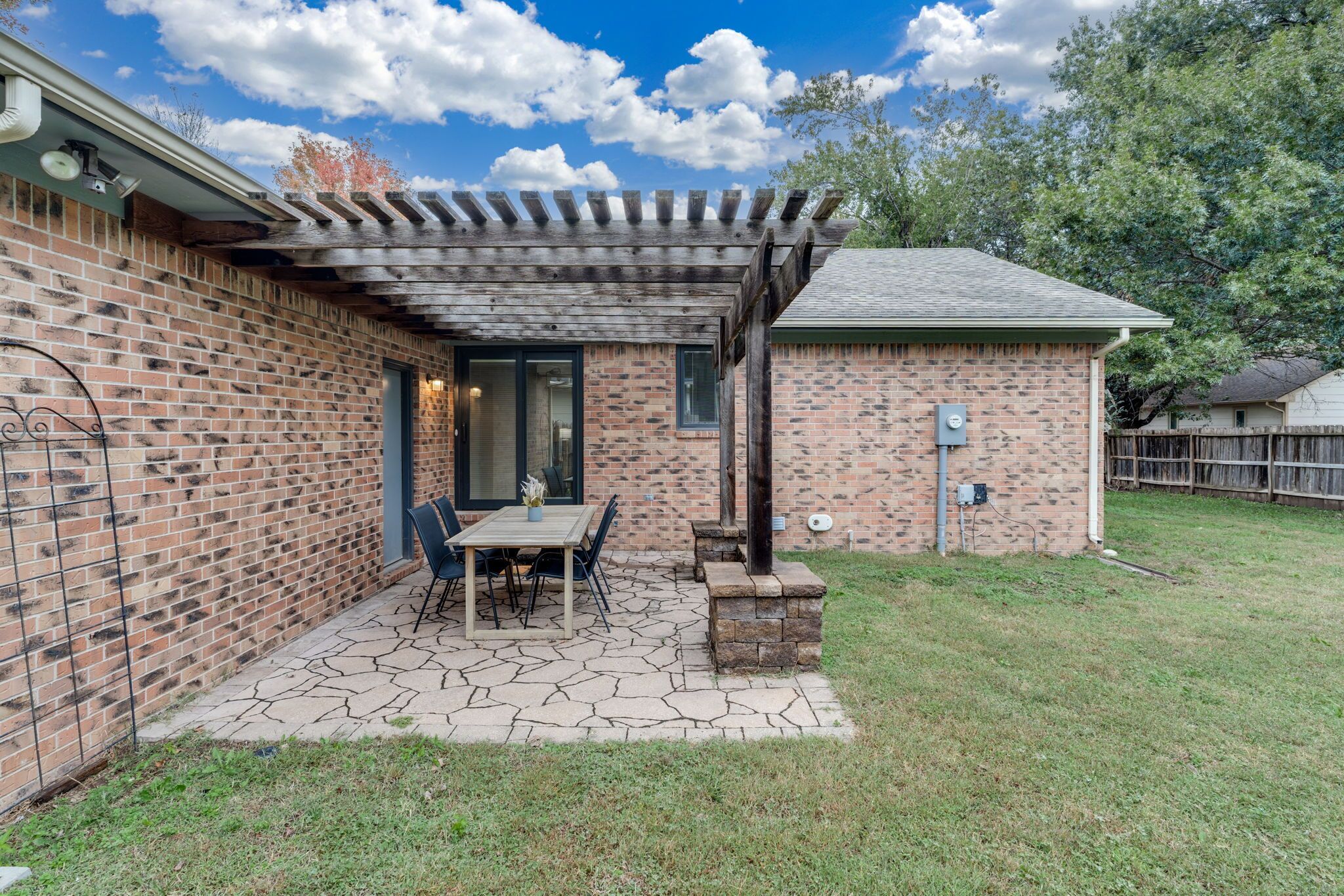 Une maison en briques avec un patio, une pergola et un petit espace extérieur aménagé pour s’asseoir.