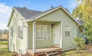 A small, single-story house with a gabled roof, a front porch with a bench, and a security camera mounted on the door.