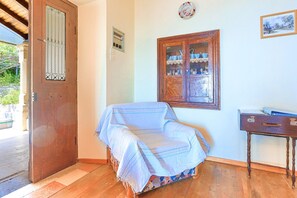 A room with a wooden door, a window with a view of a landscape, a small table with a blue cloth, and a wall-mounted electrical outlet. - Old Stone House in Nisaki (Corfu)