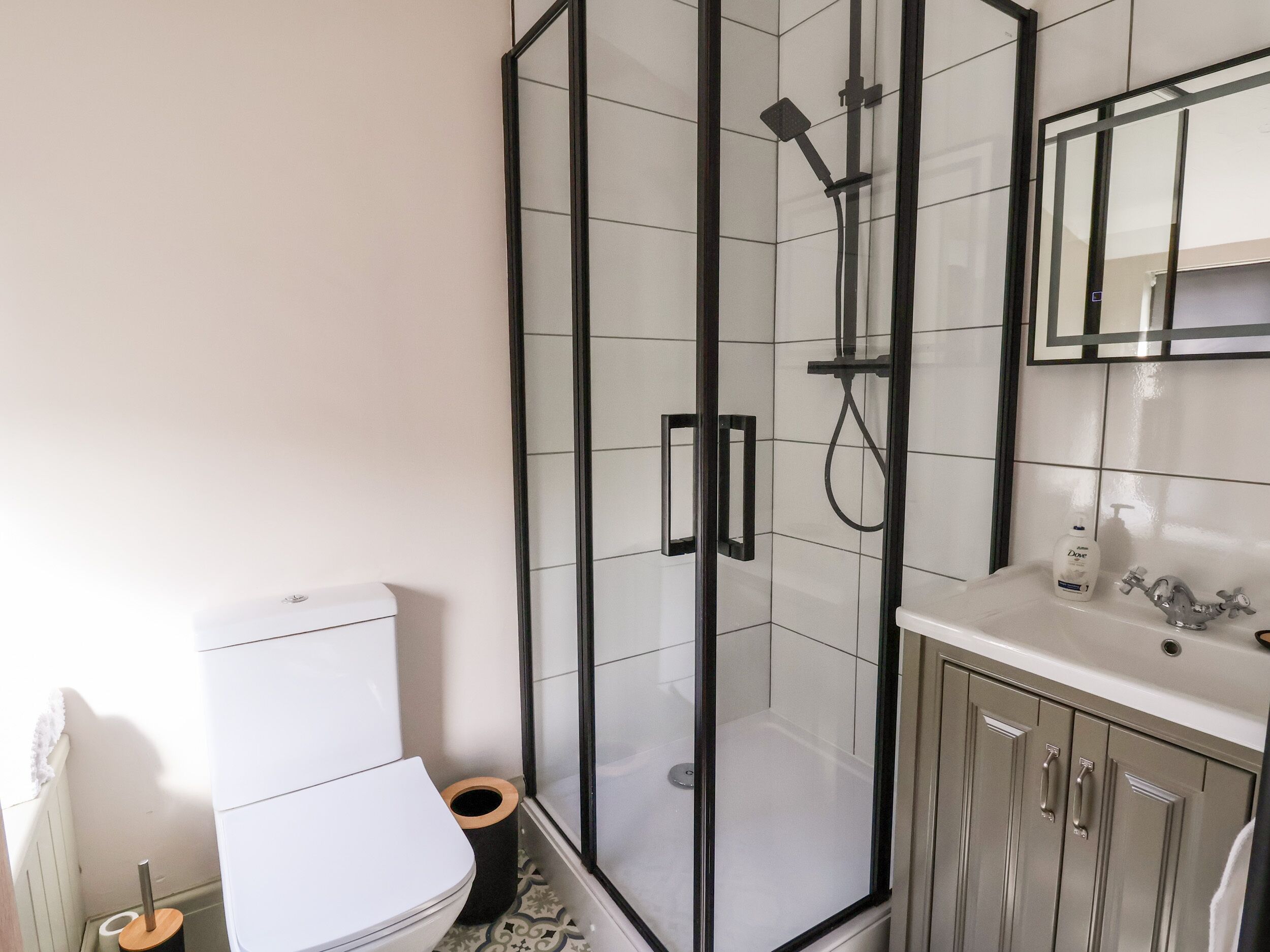 Et moderne badeværelse med et glasafskærmet brusebad, et hvidt toilet og et vaskeskrin med spejl og vask.