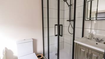 Et moderne badeværelse med et glasafskærmet brusebad, et hvidt toilet og et vaskeskrin med spejl og vask.