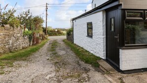 A narrow gravel path leading to a white building with a black door and windows. - 3 Penllan Cottages (Holywell)