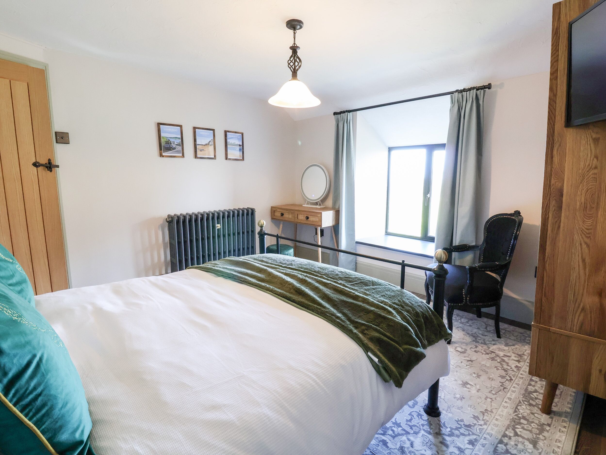 A bedroom with a bed, a wooden wardrobe, a desk with a mirror, and a window with curtains.