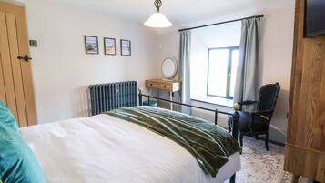 A bedroom with a bed, a wooden wardrobe, a desk with a mirror, and a window with curtains.
