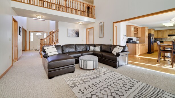 A spacious living room with a large sectional sofa, a round ottoman, and a patterned rug. A staircase leads to an upper level with a balcony. - Cozy Spacious Luxury Home with lots of Positivity Energy! (Tobyhanna)