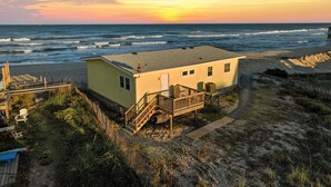 Una casa davant de la platja amb terrassa de fusta, un petit porxo i vista a l'oceà.