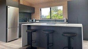 Une cuisine moderne dotée d’un grand îlot central, d’appareils électroménagers en acier inoxydable et offrant une vue sur la verdure environnante.