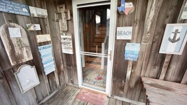 A wooden beach house entrance with various signs and a welcome mat. - GENTLE BREEZE is Close to Beach in POC (Port O Connor)