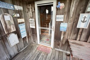 L’entrée d’une maison de plage en bois, agrémentée de divers panneaux et d’un paillasson de bienvenue.